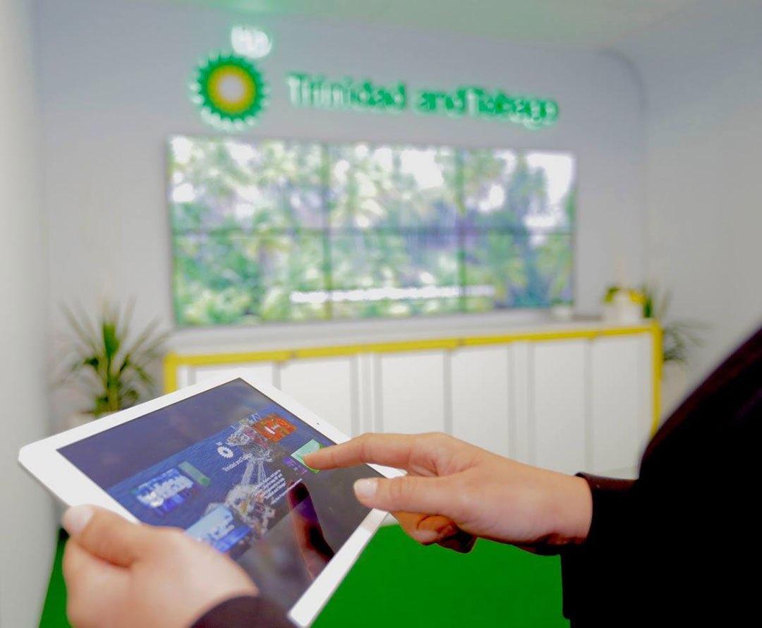 A visitor using the BP conference application on an iPad in front of the exhibition video wall.